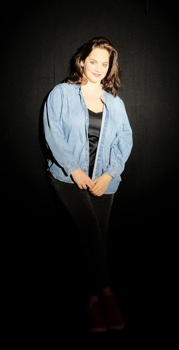 Isabelle Farah in a denim shirt, standing in a spotlight